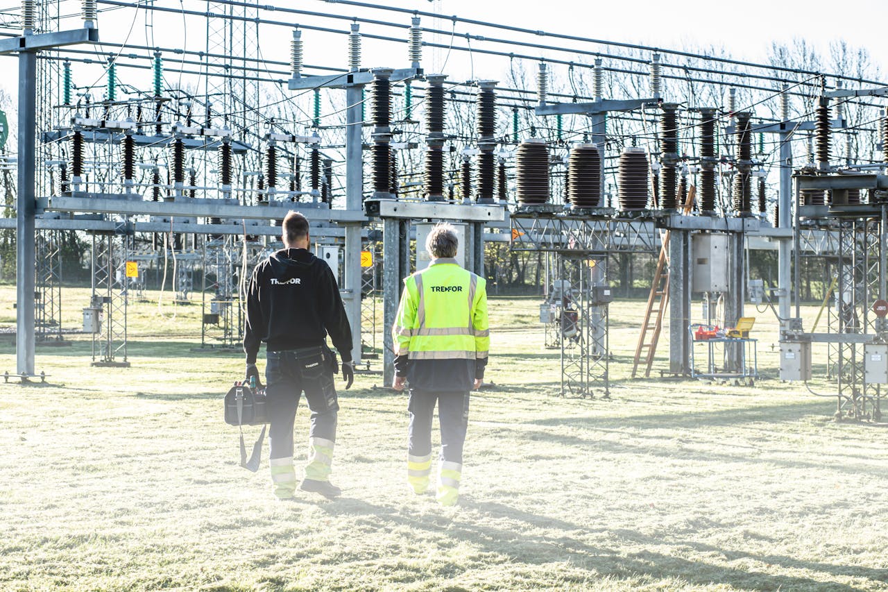 my-path Two workers inspect an outdoor electrical substation, emphasizing safety and maintenance.