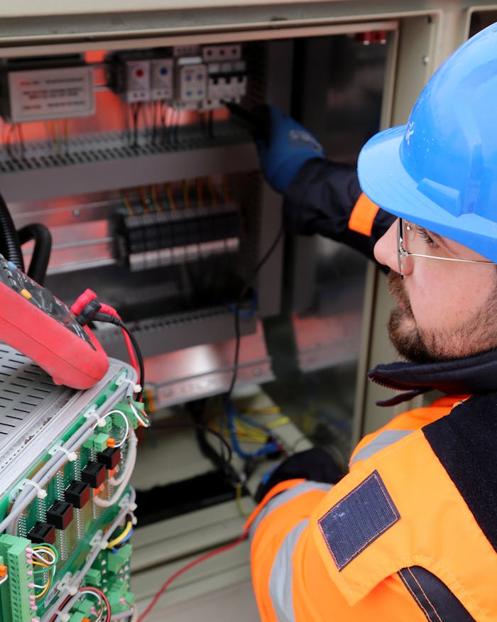 pexels-photo-17842834 Electrician wearing safety gear operates switchboard in industrial setting.