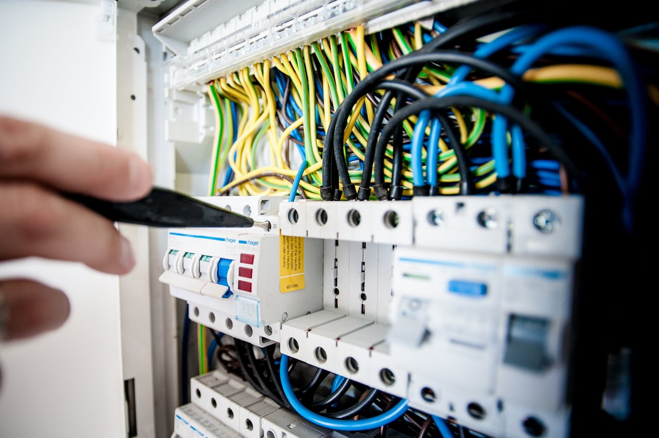 about-me-img Hand of electrician working on a circuit breaker panel with colorful wires, ensuring safe electrical connections.