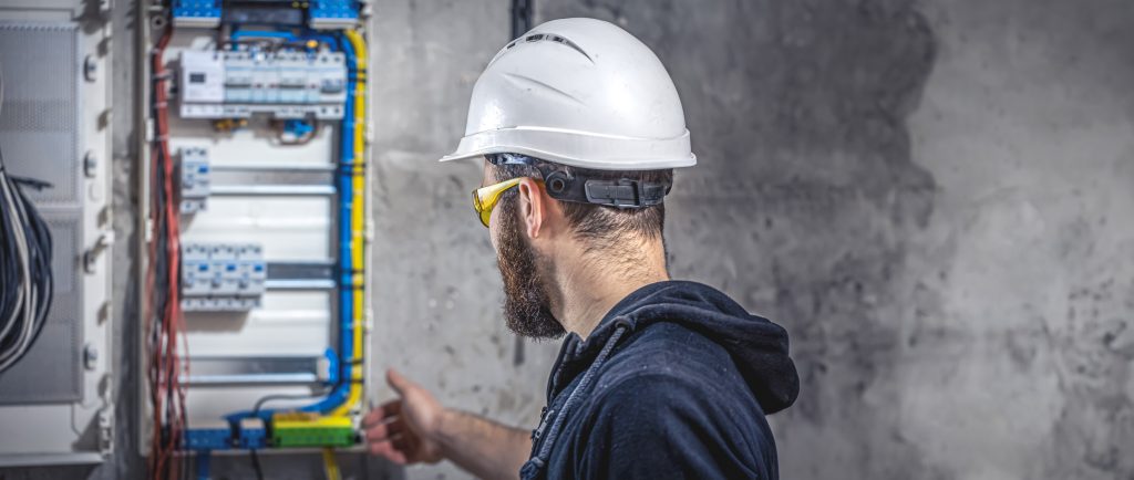 A male electrician works in a switchboard with an electrical connecting cable.